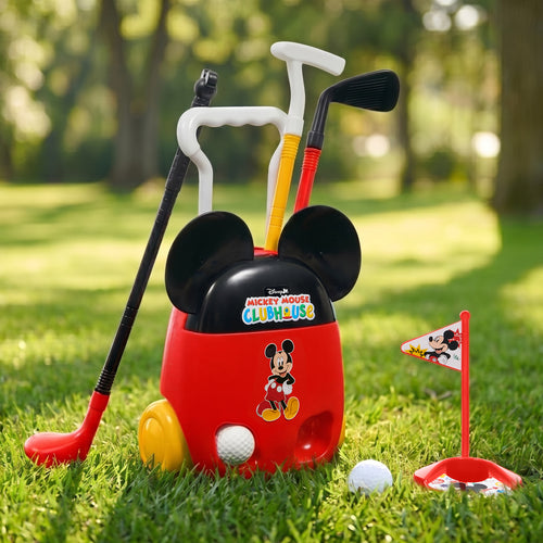 A Mickey Mouse Clubhouse golf toy set on a grassy lawn, featuring a red and black rolling cart with Mickey graphics, three golf clubs, a small flag, and golf balls, photographed outdoors in a park.