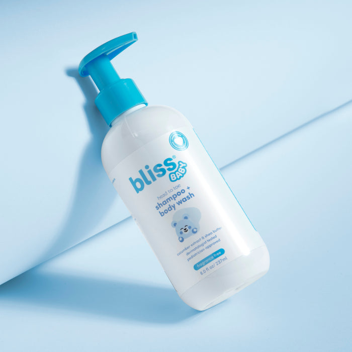 A bottle of 'Bliss' baby shampoo and body wash on a bathtub surrounded by yellow rubber ducks and a blue washcloth. 1-Head to Toe - Shampoo + Body Wash