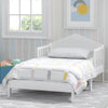 White children's bed with colorful bedding in a room with a window and wall art. 7-Homestead Toddler Bed