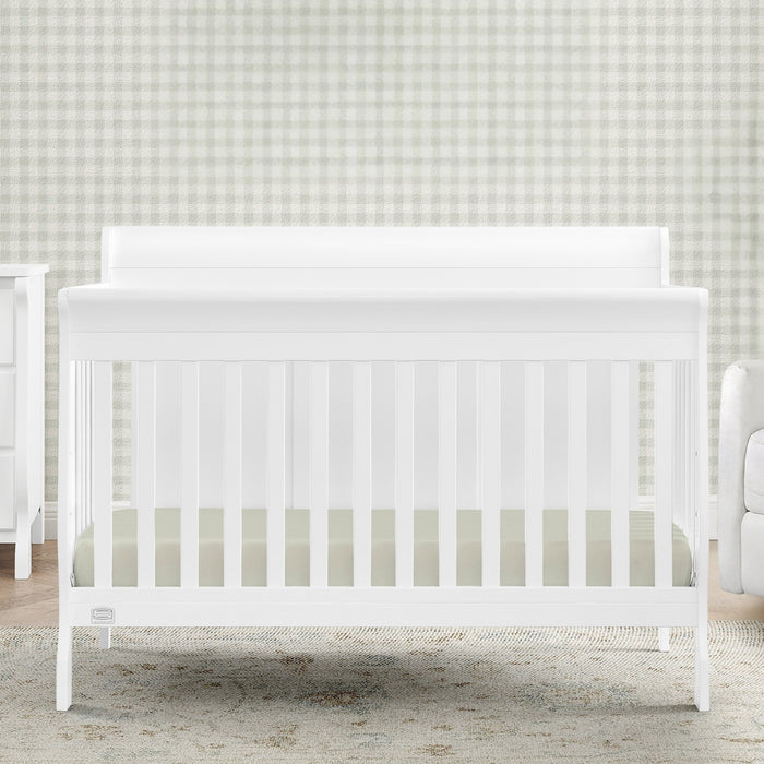 White crib in a room with a checkered wall and furniture. 2-Carter 6-in-1 Convertible Crib