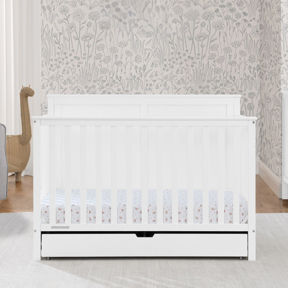 White crib with a floral patterned wall in the background