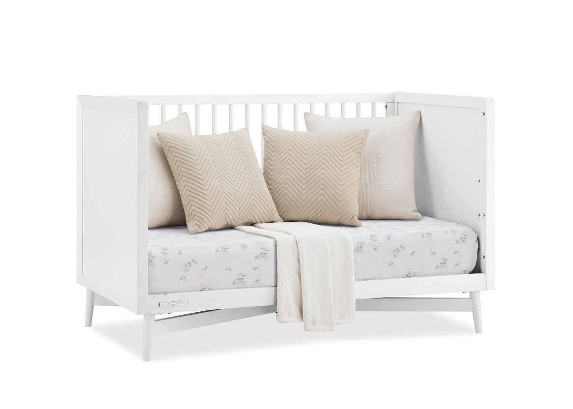 White daybed with beige pillows and a blanket on a white background