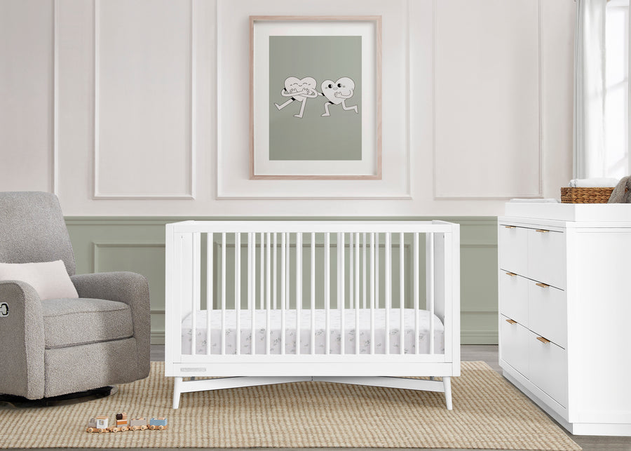 Nursery room with a white crib, gray armchair, and framed artwork on the wall. 21-Dylan 4-in-1 Convertible Crib