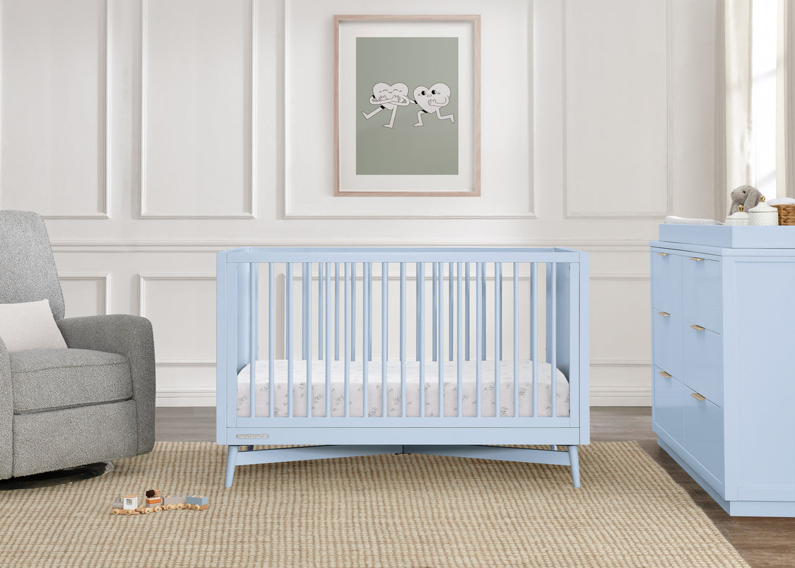 Nursery with light blue crib and dresser against a white paneled wall.
