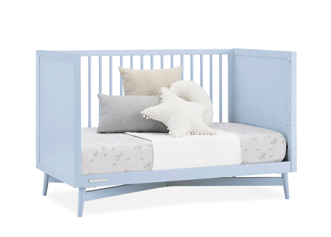 Light blue crib with bedding and pillows on a white background
