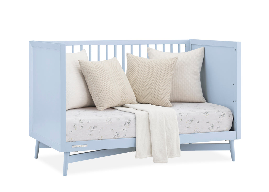 Light blue crib with white bedding and pillows on a white background