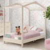 Child playing on a pink bed with a white canopy in a room with floral wallpaper. 34-Poppy House Twin Bed