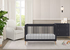Nursery room with a black crib and white armchair near a window. 16-Jordan 4-in-1 Convertible Crib