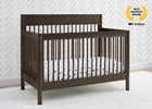 Wooden crib with white crib sheet against a white wall with a geometric pattern 24-Remy 6-in-1 Convertible Crib
