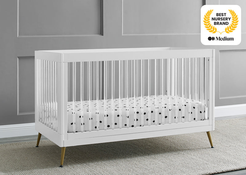 White crib with a polka dot mattress in a room with gray walls and a gray carpet.