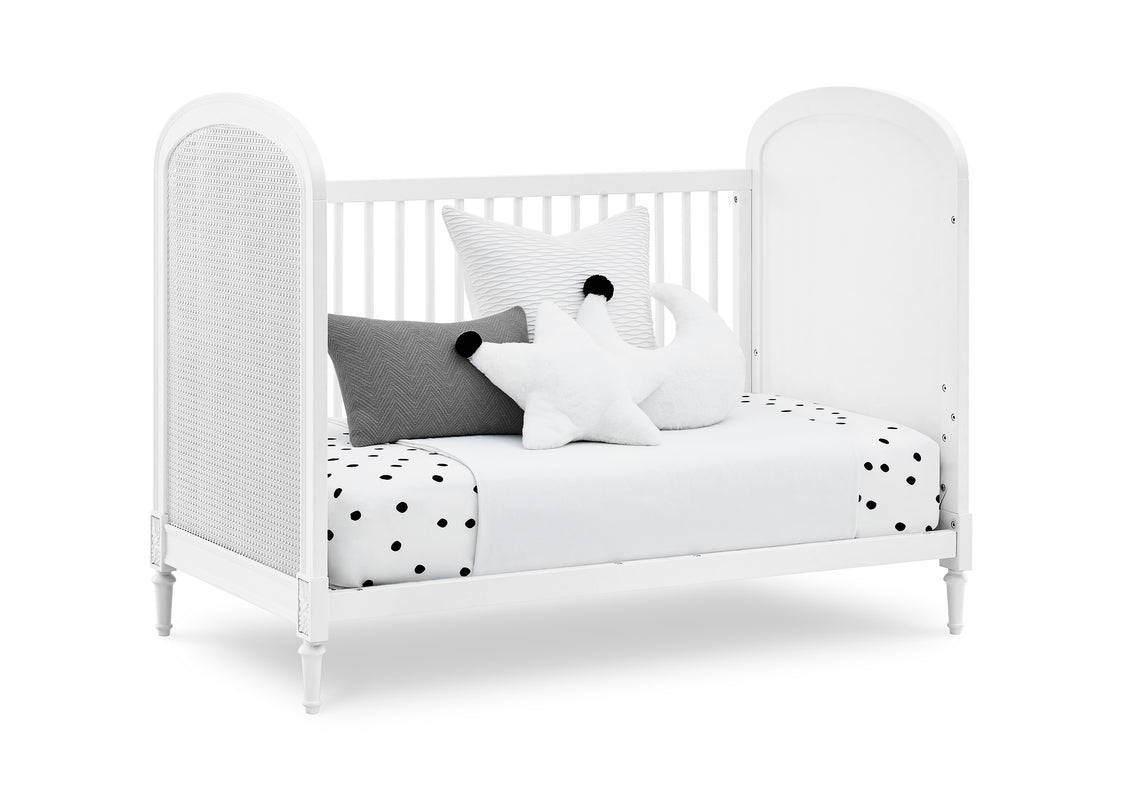 White crib with polka dot bedding and pillows on a white background