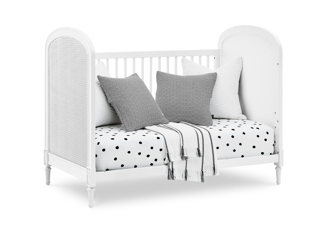 White crib with gray pillows and a polka dot blanket on a white background