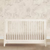 White crib in a room with decorative wallpaper featuring small illustrations of houses and trees. 2-babyGap Wren Collection
