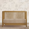 Wooden crib with white bedding against a wallpapered wall 1-babyGap Wren Collection