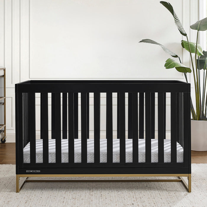Black crib in a room with 'River Grace' wall art and plants. 1-Jade 4-in-1 Convertible Crib