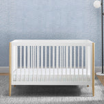 White crib with wooden sides in a room with light blue patterned wallpaper.