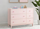 Pink dresser with pink knobs in a room setting with decor items and a plant. 9-babyGap Legacy 6 Drawer Dresser with Interlocking Drawers