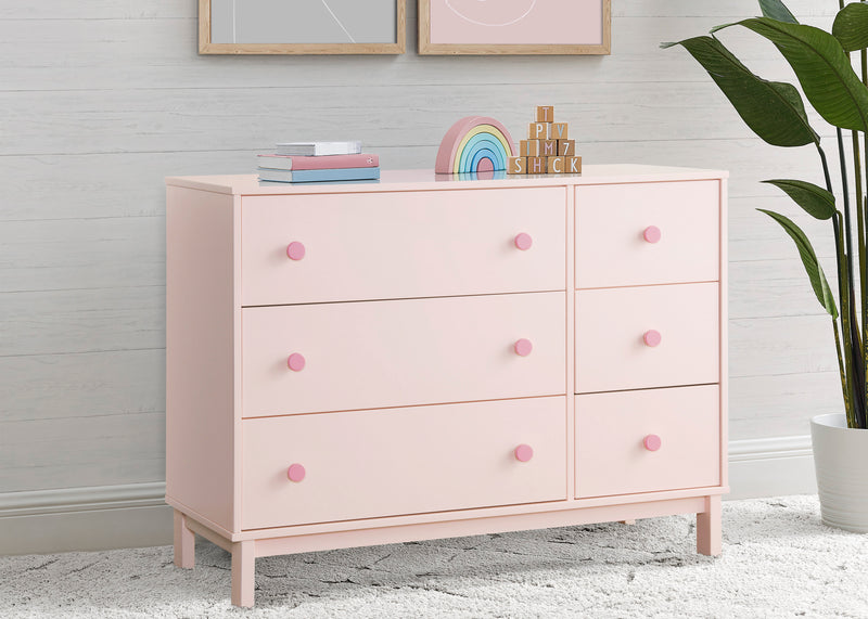 Pink dresser with pink knobs in a room setting with decor items and a plant. 9-babyGap Legacy 6 Drawer Dresser with Interlocking Drawers