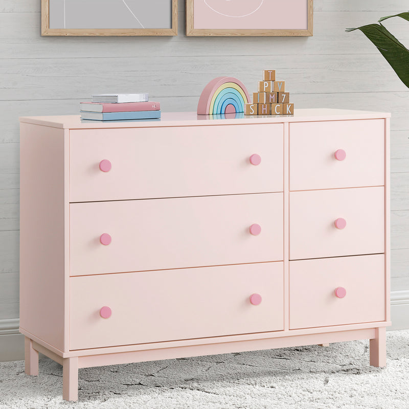 Pink dresser with colorful decor items against a light gray wall.