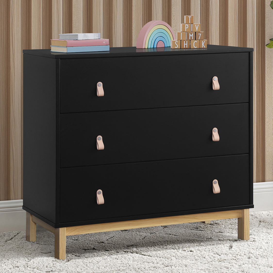 Black dresser with wooden legs and pink handles in a room setting.