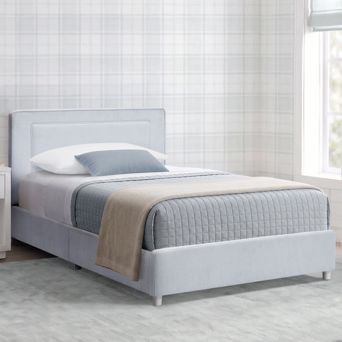 A light gray upholstered bed frame with a padded headboard and textured base, shown in a styled bedroom setting with white bedding, a blue-gray pillow, and a beige throw blanket against a plaid wallpaper background. 1-Riley Upholstered Twin Bed