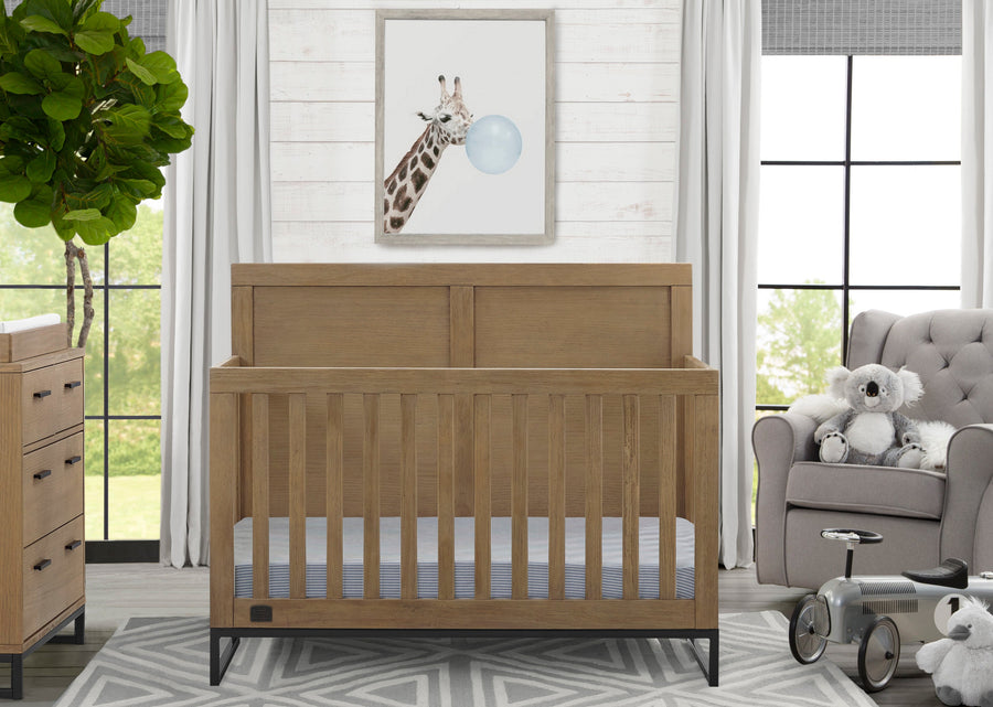 Wooden crib in a nursery with a giraffe painting on the wall and a gray chair with stuffed animals. 27-Foundry 6-in-1 Convertible Crib