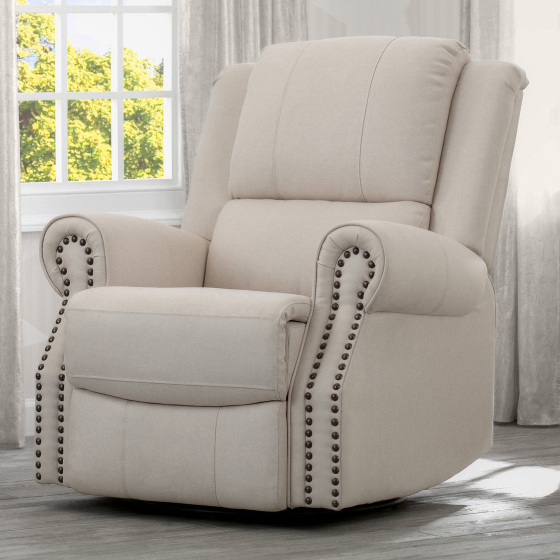 A beige upholstered recliner glider swivel chair with cushioned arms and nailhead trim, positioned in a nursery room.