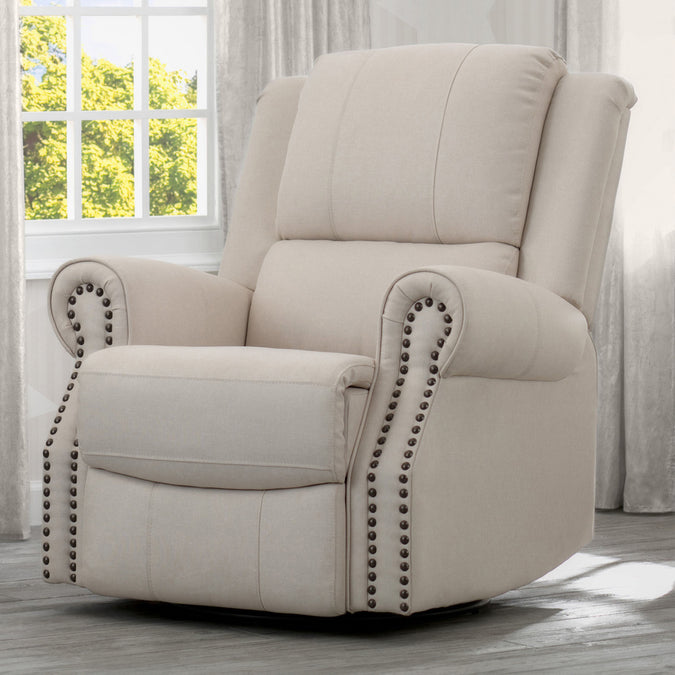 A beige upholstered recliner glider swivel chair with cushioned arms and nailhead trim, positioned in a nursery room. 6-Dylan Nursery Recliner Glider Swivel Chair
