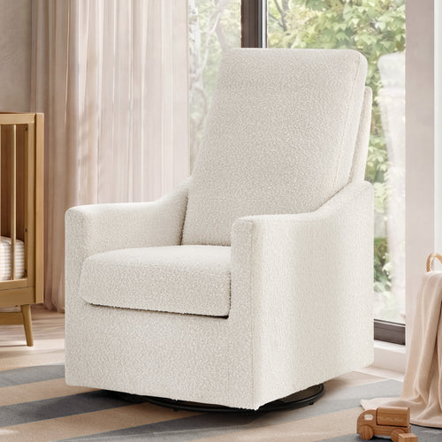 An upholstered swivel glider chair in a textured cream bouclé fabric, shown in a softly lit nursery or living room setting with curtains, a crib, and a window.