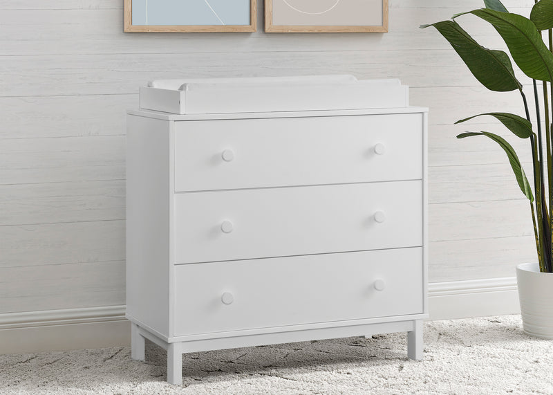 White dresser with drawers in a room with a plant and framed pictures on the wall.