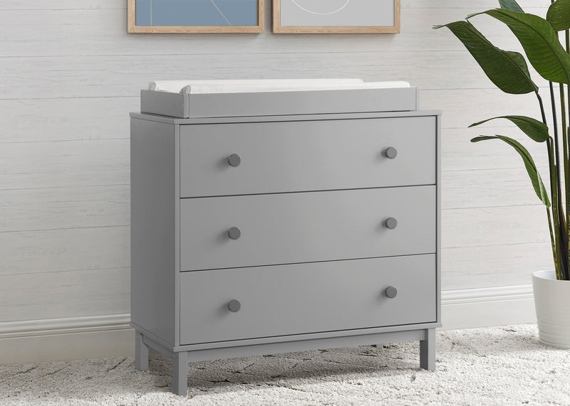 Gray dresser with a changing table top in a room with a plant and framed pictures on the wall.