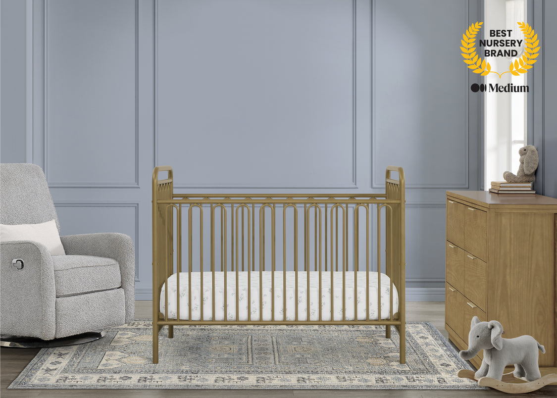Nursery room with wooden crib, gray armchair, and dresser against a gray wall.