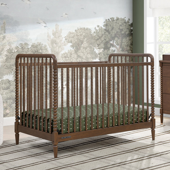 Wooden crib with green mattress in a room with large windows and greenery outside 2-Saint 4-in-1 Convertible Crib