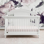 White crib in a nursery with floral wallpaper