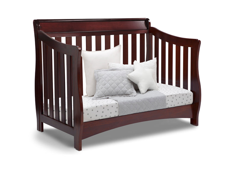 Wooden crib with white pillows and a gray quilt on a white background