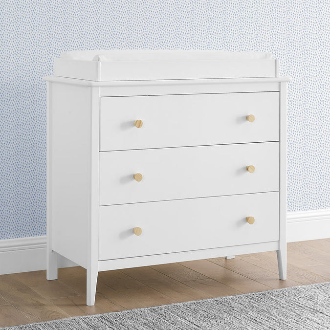 White dresser with gold knobs against a light blue wall. 13-Casey 3 Drawer Dresser with Interlocking Drawers