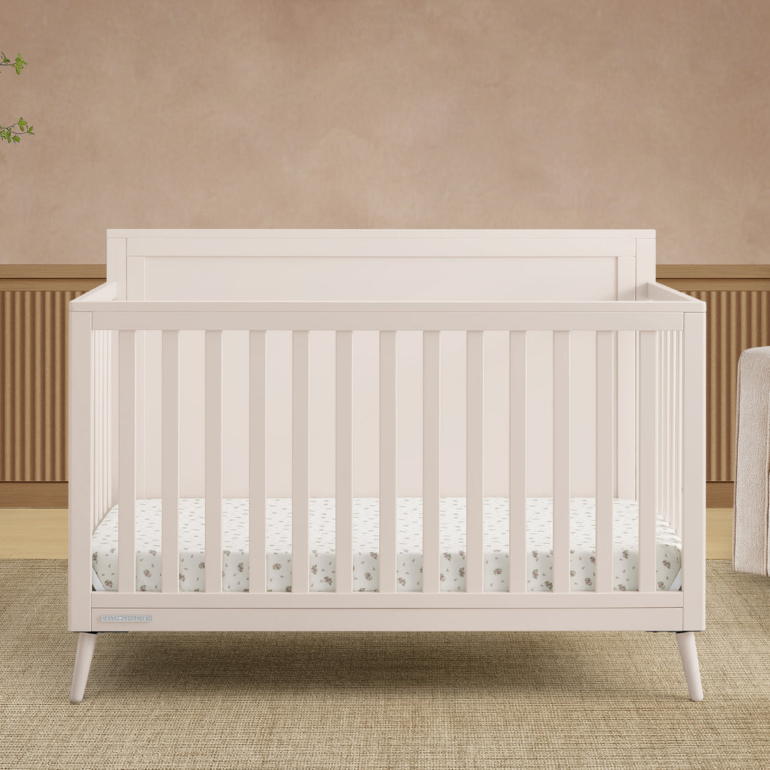 White crib in a room with beige walls and a wooden floor.