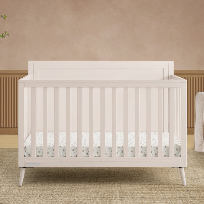 White crib in a room with beige walls and a wooden floor. 26-Lola 6-in-1 Convertible Crib