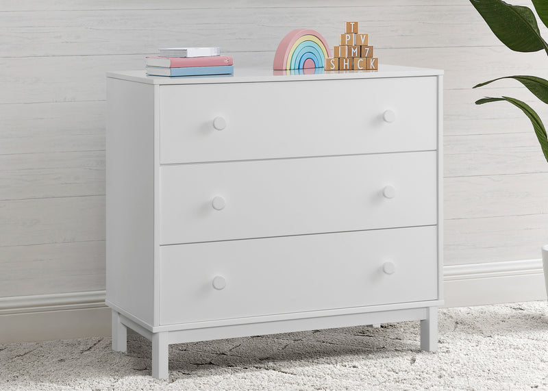 White dresser with three drawers against a light wooden paneled wall.