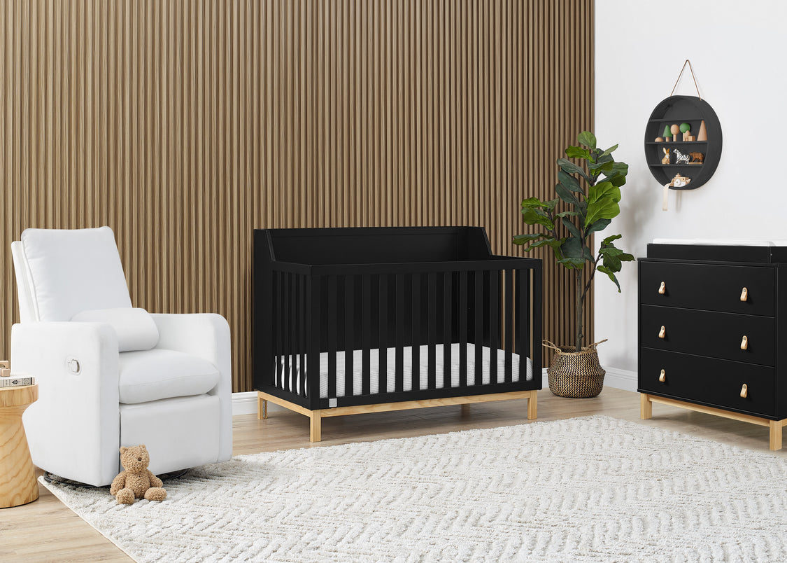 Nursery room with black crib, white armchair, and wooden dresser.