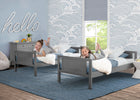 Two children playing on gray beds in a room with blue walls and decorative elements. 14-Convertible Twin Bunk Bed with Ladder and Guardrails