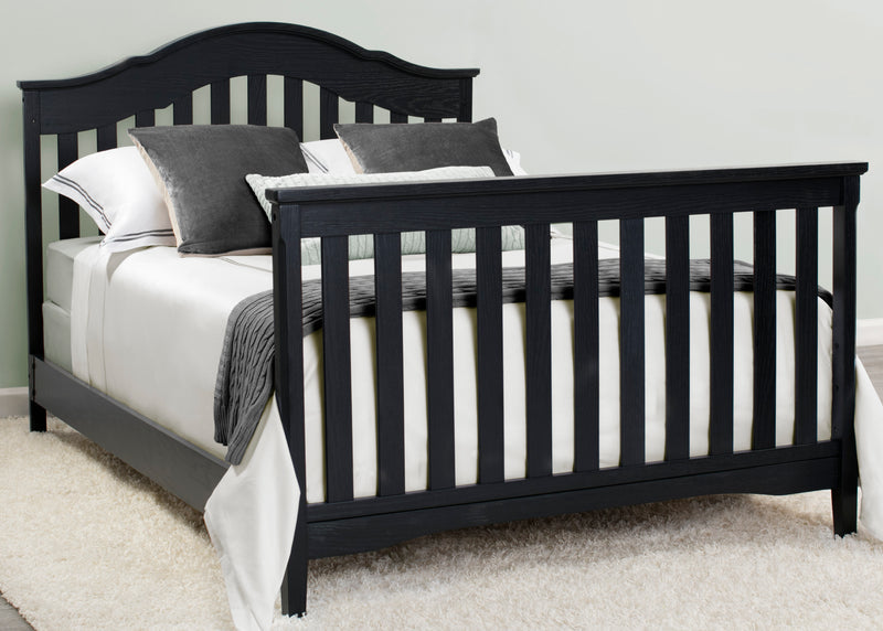 Black crib with white bedding and gray pillows in a room setting. 28-Farmhouse 6-in-1 Convertible Baby Crib