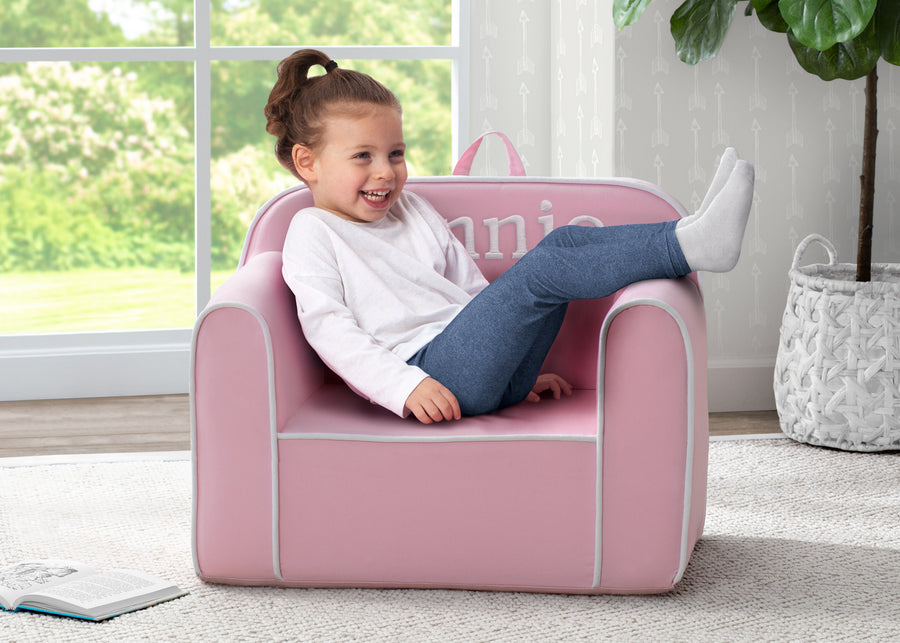 A child sitting on a pink foam chair with the name 'UNICEF' personalized on the backrest. 1-Personalized Cozee Chair For Kids