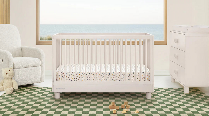 White crib in a nursery with a teddy bear and toys on a checkered floor. 3-Ari Collection