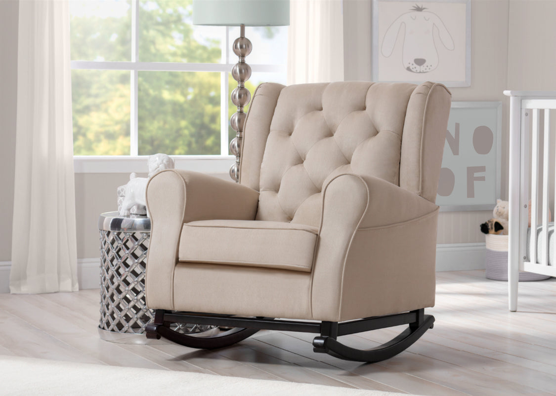 Beige rocking chair in a room with a crib and lamp.