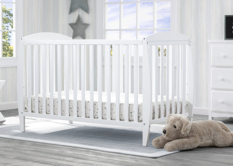 White crib in a bright nursery with a teddy bear on the floor. 23-Taylor 4-in-1 Convertible Crib