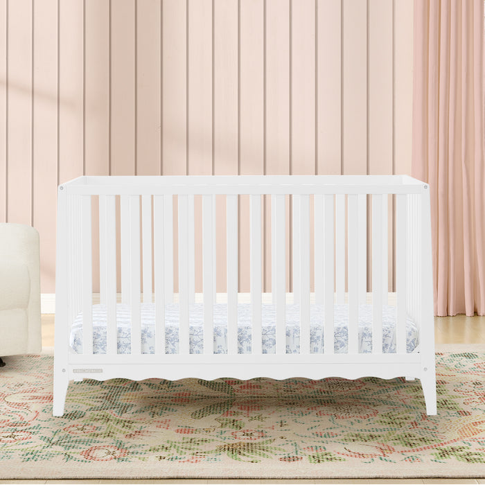 White crib in a room with a pink curtain and patterned rug 1-Lulu 5-in-1 Convertible Crib