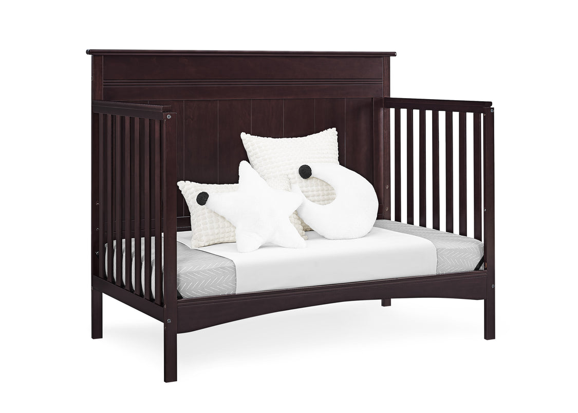 Dark wood crib with white bedding and decorative pillows on a white background
