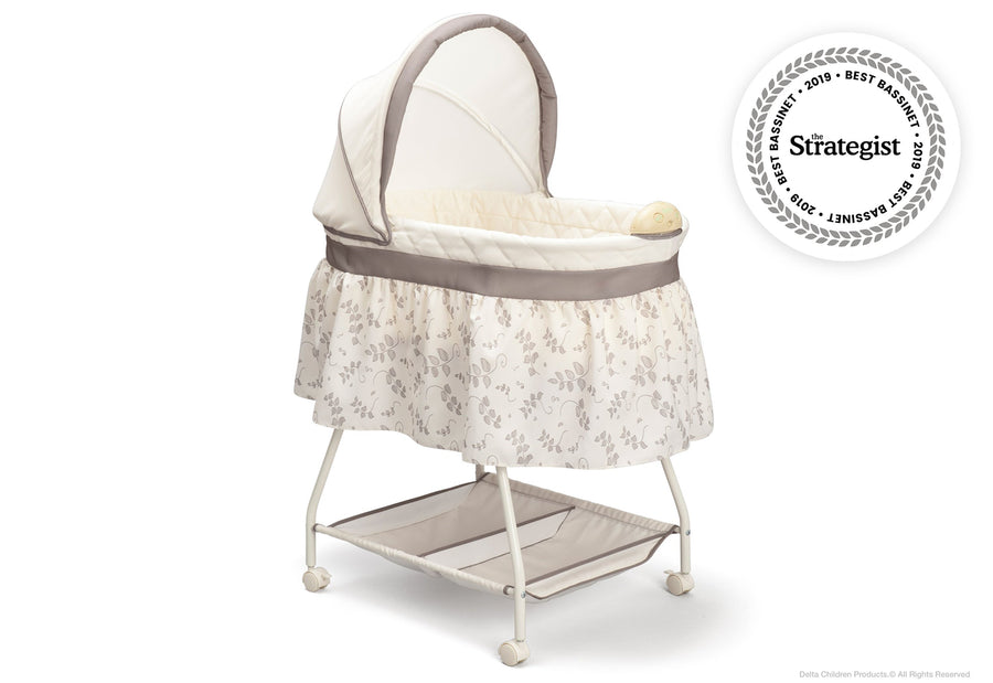 A white and beige Deluxe Sweet Beginnings Bassinet with a fitted sheet, removable canopy, storage basket underneath, and locking wheels. 1-Deluxe Sweet Beginnings Bassinet